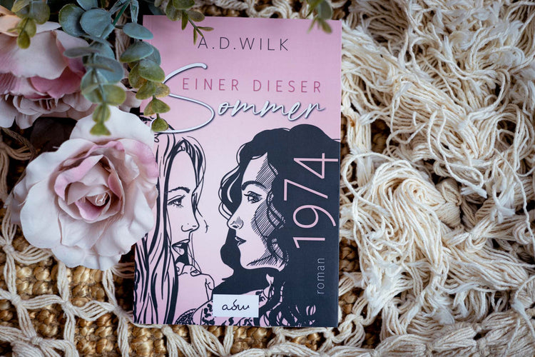 Taschenbuch »1974. Einer dieser Sommer.« von A.D. WiLK mit Eukalyptuszweig auf heller Strickdecke, in Szene gesetzt.